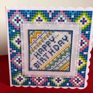 Happy Birthday in cross stitch on a white card.