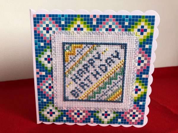 Happy Birthday in cross stitch on a white card.