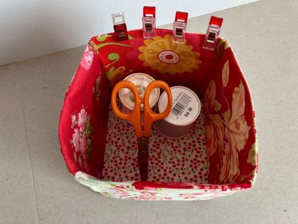 Fabric storage box in shades of red with thread, scissors and clips